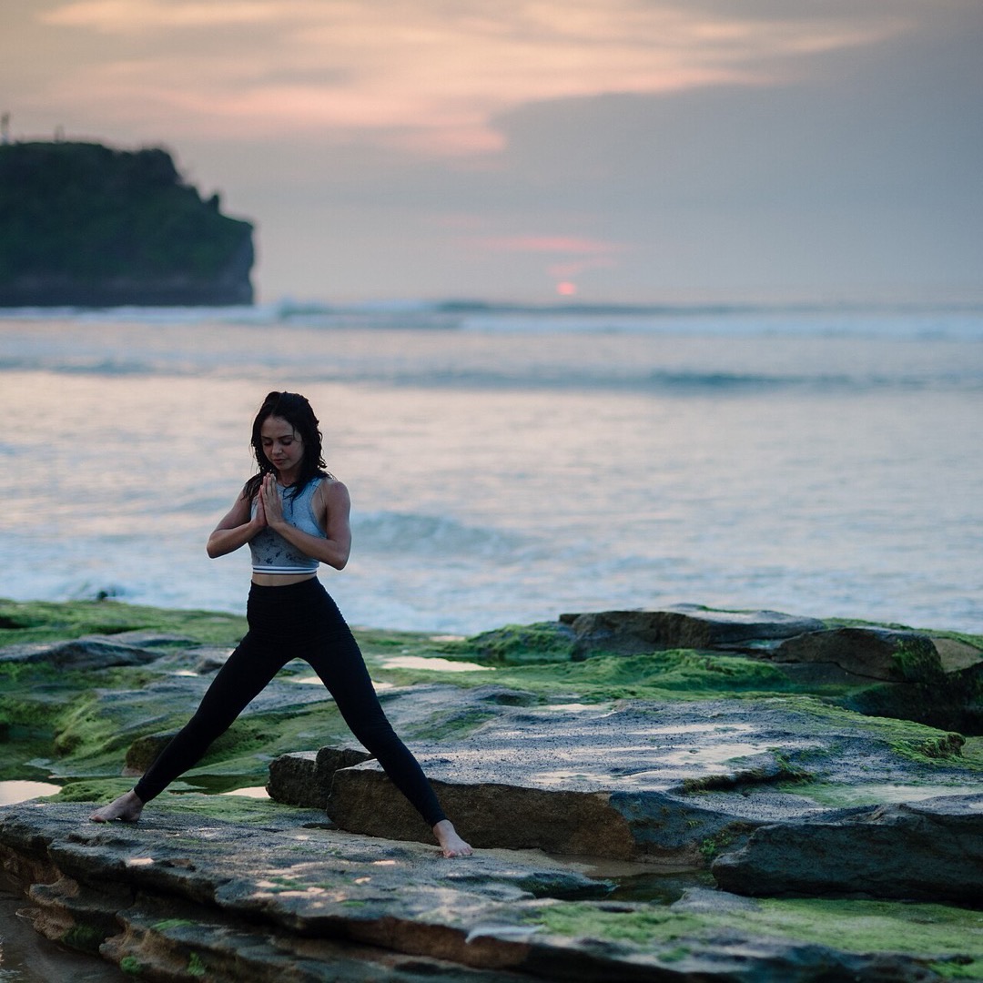 A woman in a serene yoga pose on rocks by the ocean at sunset